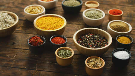 Arrangement of colorful spices and condiments in various bowls on shabby wooden table in daylightの写真素材