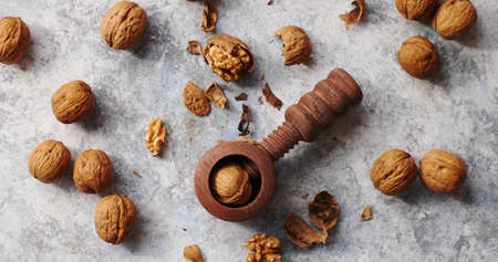 Flat lay of rustic wooden cracker for nuts on marble table surface with golden walnuts and shells