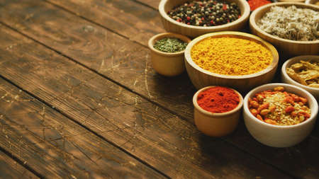 Collection of various spices and condiments in small bowls arranged on shabby wooden tableの写真素材