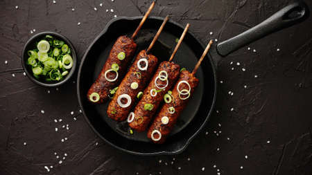 Barbecued turkey kebab decorated with fresh onion and chive in frying pan, top view. Black stone background.の写真素材