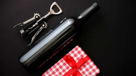 Red wine bottle, corkscrew and boxed christmas gift on black matte background. Top view with copy spaceの写真素材
