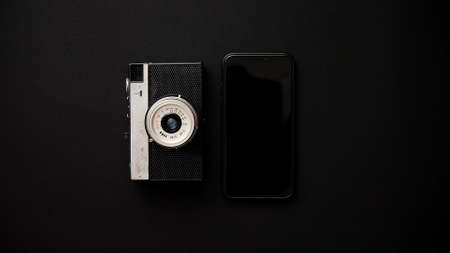 Old retro film camera and modern smartphone next to each other lying on black background. Top view.の写真素材