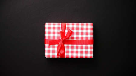 Gift box wrapped with red checkered pattern christmas paper with red bow on black table, top view