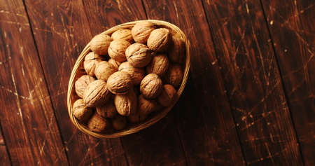 From above shot of bowl with whole fresh walnuts standing on scratched surface of wooden tabletop