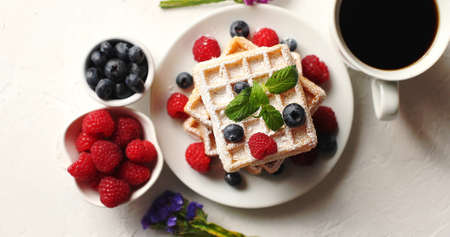 From above shot of cup of aromatic coffee and bowls with fresh berries standing near plate with delicious soft wafflesの写真素材