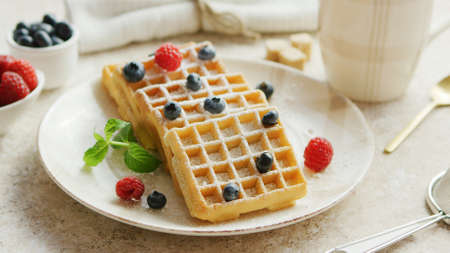 Closeup shot of ceramic plate with tasty soft waffles and ripe berries standing on marble tabletop