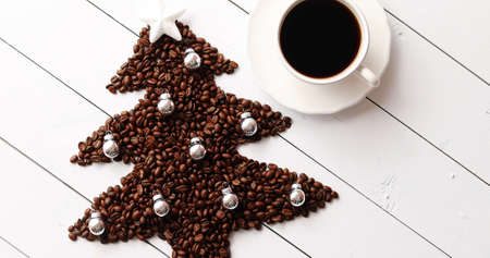 From above view of brown beans in shape of Christmas tree and cup of black coffee on white wooden backgroundの写真素材