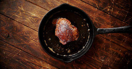 From above view of fresh fried meat in cooking oil placed on black pan on wooden background