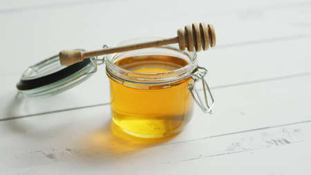 Glass jar full of honey with spindle on white wooden background