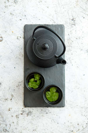 Traditional eastern metal teapot and iron cups with mint tea leafs placed on stone plate. Over the white rusty stone backgroundの写真素材