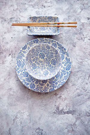 Empty traditional set tableware from Asia. Chopsticks, bowl, plate and soy souce dish placed on stone background with copy space.の写真素材