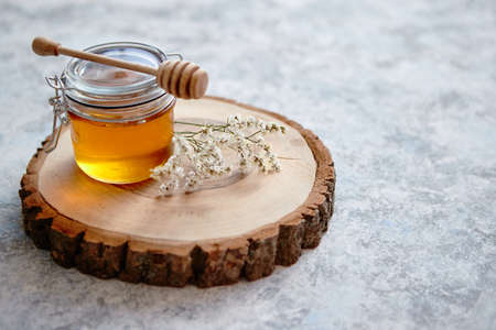 Glass jar full of fresh honey placed on slice of wood. Stone background with copy space.の写真素材