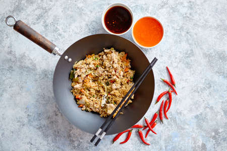 Delicious fried rice with chicken. Prepared and served in a wok with soy and sweet sour souces on side. Placed on stone background. Top view.の写真素材