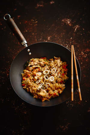Delicious fried rice with chicken. Prepared and served in a wok with soy and sweet sour souces on side. Placed on dark rusty background. Top view.の写真素材