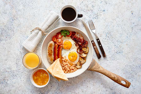 Full English Breakfast served in a pan. Fried eggs, beked beans, tomatoes, champignons, crispy bacon, sausages and toast. Placed on stone background. Top view with copy space.の写真素材