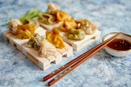 Delicious mixed kinds of chinese dumplings served on wooden stands with chopstick and soy sauce. Placed on stone background with copy space.の写真素材