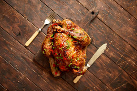 Homemade roasted spicy chicken with chilli and chive. Served on dark brown chopping board. Old wooden background, Shot from above.の写真素材