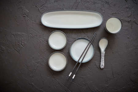 Set of empty ceramic dishes for sushi and rolls on a black stone table. Chopstick cup, plate, small...