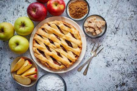 Delicious apple pie cake with a fresh red and green apples fruits, brown and powder sugar. Placed on rusty scratched stone table.の写真素材