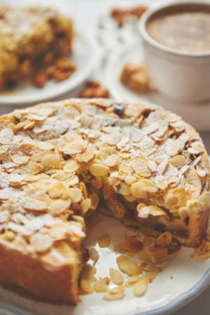 Vertical shot of a whole round delicious apple cake tart with almond flakes served on wooden table. With coffee in a cup and slice of a pie on soucer.の写真素材