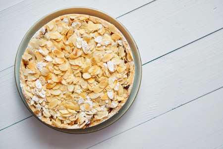 Homemade apple cake sprinkled with almond flakes and icing sugar. Placed on white wooden table