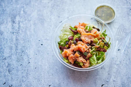 A delicious smoked salmon take away salad with smoked salmon, lettuce, mixed baby greens, beans, dry tomatoes, cherry tomatoes and red onion with green sauce.の写真素材