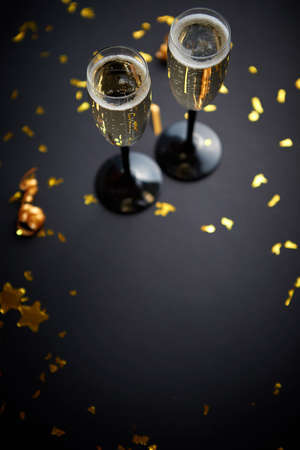 Two glasses full of sparkling champagne wine with golden decoration of confetti and serpentines on black elegant background. Top view with copy space. Festive or party concept.の写真素材