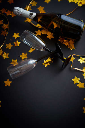 Glasses and bottle of champagne with golden serpentines and confetti lying on black background. New Year or party celebration concept. Top view. Flat lay.の写真素材