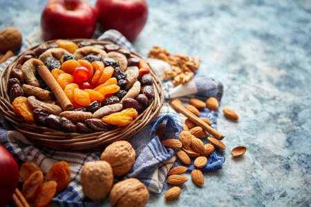 Composition of dried fruits and nuts in small wicker bowl placed on a stone table. Assortment contais almonds, walnuts, apricots, plums, figs, dates, cherries, peaches. Above view with copy space.の写真素材
