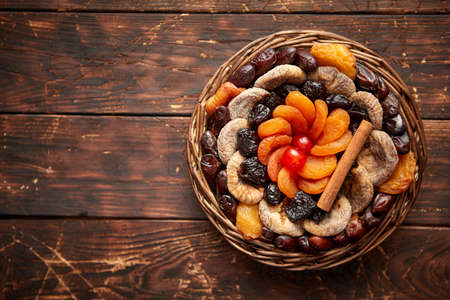 Mix of dried fruits in a small wicker basket on wooden table. Assortment contais apricots, plums, figs, dates, cherries, peaches. Above view with copy space.の写真素材