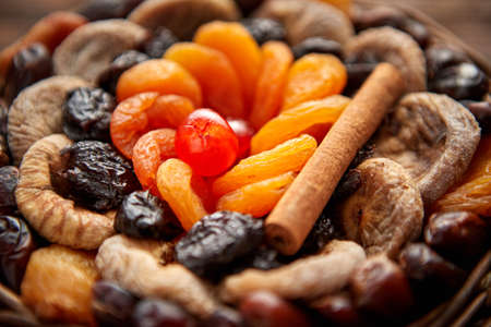 Close up of mix of dried fruits in a small wicker basket on wooden table. Assortment contais apricots, plums, figs, dates, cherries, peaches. Above view with copy space.の写真素材