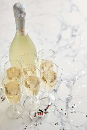 Champagne glasses and bottle placed on white marble background. Party and holiday celebration concept with confetti and serpentines. With copy space.の写真素材