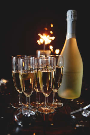 Party composition image. Glasses filled with champagne placed on black table. With bottle of wine and sparkler. Elegant composition with copy space.の写真素材