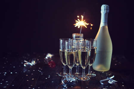 Party composition image. Glasses filled with champagne placed on black table. With bottle of wine and sparkler. Elegant composition with copy space.の写真素材