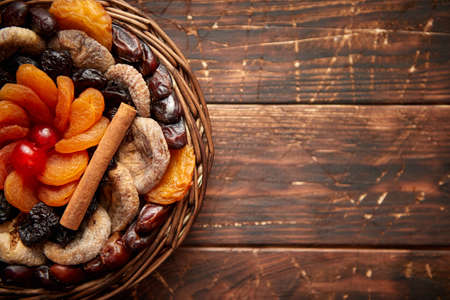 Mix of dried fruits in a small wicker basket on wooden table. Assortment contais apricots, plums, figs, dates, cherries, peaches. Above view with copy space.の写真素材