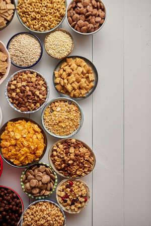 Assortment of different kinds cereals placed in ceramic bowls with cornflakes, granola, cereals and oatmeal. The concept of breakfast food. Flat lay, with copy space, top view on white wooden table.の写真素材