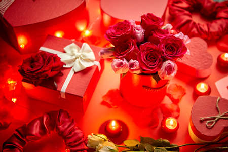 Valentines day romantic decoration with roses, boxed gifts, candles, on a red background table. Top view, copy space.の写真素材