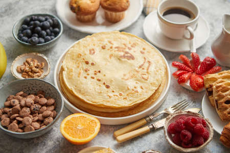 Breakfast table setting with fresh fruits, pancakes, coffee, croissants, sweet cakes, muffins. Flat...
