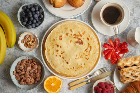 Breakfast table setting with fresh fruits, pancakes, coffee, croissants, sweet cakes, muffins. Flat...