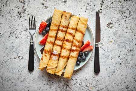 Plate of delicious crepes roll with fresh fruits and chocolate placed on rusty table. Top view, flat lay.の写真素材