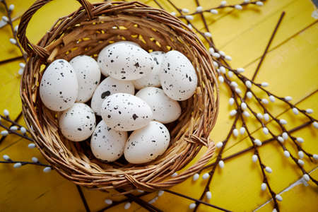 Whole chicken eggs in brown wicker basket. The concept of Easter Holidays. Yellow wooden background. Flat lay, top view.の写真素材
