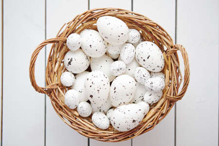 Basket of chicken and quail white dotted Easter eggs in brown wicker basket. Placed on white wooden table.の写真素材