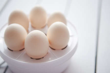 Chicken eggs in a egg electric cooker on a white wooden table ready for boiling.の写真素材