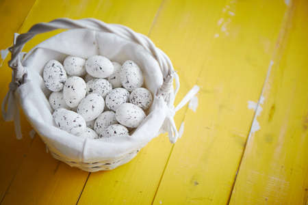 Quail eggs In white wicker basket. The concept of Easter Holidays. Yellow wooden background. Flat lay, top view.の写真素材