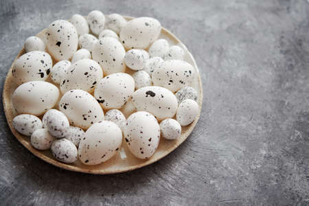 Composition of white traditional dotted Easter eggs in white ceramic plate placed on gray stone background. High angle shot.の写真素材