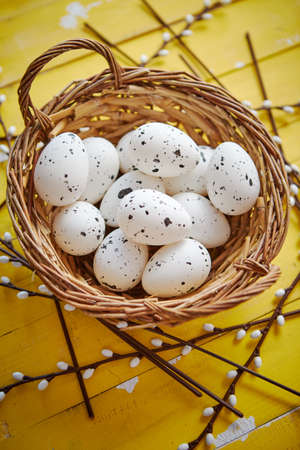 Whole chicken eggs in brown wicker basket. The concept of Easter Holidays. Yellow wooden background. Flat lay, top view.の写真素材