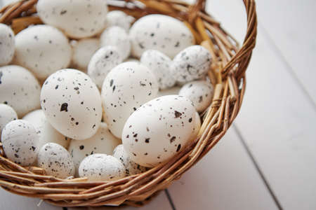 Basket of chicken and quail white dotted Easter eggs in brown wicker basket. Placed on white wooden...