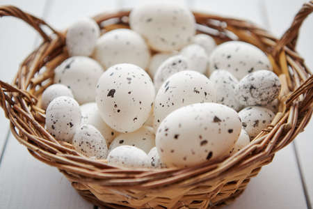 Basket of chicken and quail white dotted Easter eggs in brown wicker basket. Placed on white wooden...
