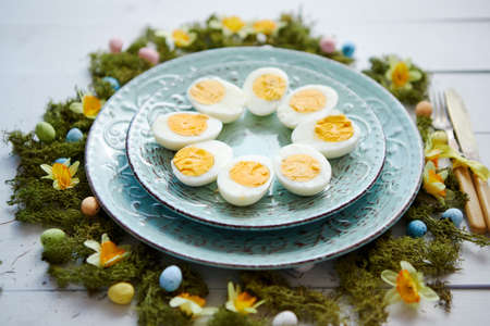 Easter table setting with flowers and eggs. Decorative ceramic plates with boiled eggs halfs. Rustical dishware. View from above.の写真素材