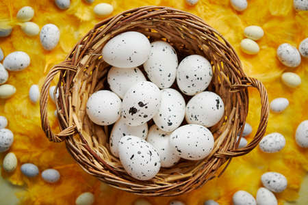 Easter holidays concept. White dotted chicken Eggs in the wicker brown nest and spring yellow feather background as a decoration. Flat lay, top view.の写真素材